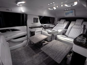 Luxe Cadillac-busje-interieur met leren stoelen, voetsteunen, ingebouwde schermen en een verfrissingsruimte.
