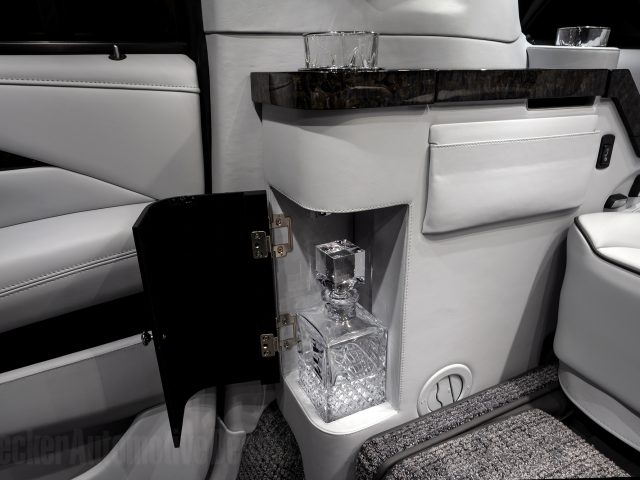 Interieur van een op maat gemaakte Cadillac met een ingebouwde kristallen karaf in een compartiment, met zachte lederen stoelen en elegante details.