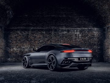 De Aston Martin 007 Edition geparkeerd in een slecht verlichte bakstenen tunnel, waarbij het slanke achterprofiel en de dubbele uitlaten goed tot hun recht komen.