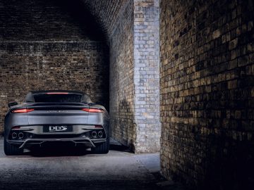 Aston Martin 007 Edition DBS geparkeerd in een slecht verlichte bakstenen tunnel, vanaf de achterkant gezien.