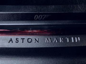 Close-up van de achterkant van een Aston Martin 007 Edition met "007"-logo en handelsmerk op koolstofvezeltextuur.