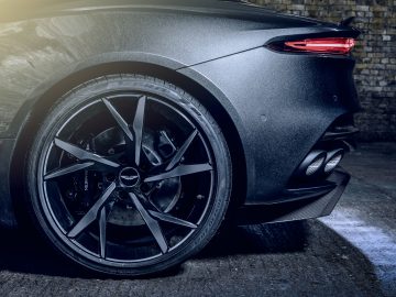 Achteraanzicht van een donkere luxeauto van Aston Martin 007 Edition, waarbij het stuur, de uitlaat en het achterlicht worden benadrukt, geparkeerd op een geplaveide ondergrond.