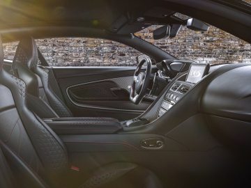 Binnenaanzicht van de Aston Martin 007 Edition, met het stuur, het dashboard en de lederen stoelen waar zonlicht naar binnen stroomt.