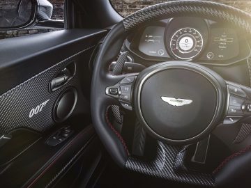 Stuur en dashboard van een Aston Martin 007 Edition luxeauto met logo, moderne instrumenten en koolstofvezeldetails.