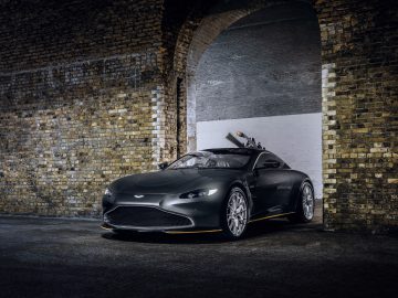 Een donkerblauwe Aston Martin 007 Edition-auto geparkeerd onder een slecht verlichte bakstenen boog, wat het strakke ontwerp en het glanzende oppervlak benadrukt.