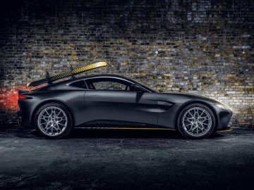 Een zwarte Aston Martin 007 Edition-sportwagen met een surfplank erop, geparkeerd tegen een bakstenen muur, verlicht door sfeerverlichting.