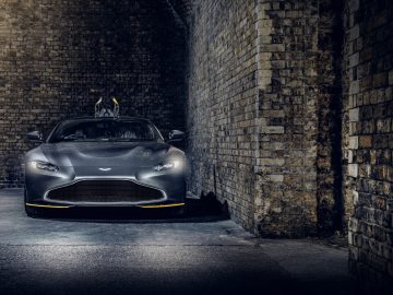 Een donkergrijze Aston Martin 007 Edition-sportwagen geparkeerd in een sfeervolle bakstenen tunnel, subtiel verlicht door bovenlichten.