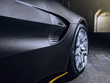 Close-up van het matzwarte zijpaneel en wiel van een Aston Martin 007 Edition-sportwagen, geaccentueerd door sfeerverlichting.