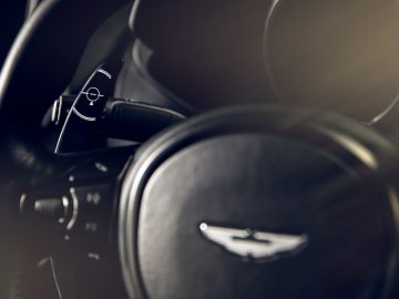 Close-up van een Aston Martin 007 Edition-stuur en bedieningshendels, met een wazig dashboard op de achtergrond.