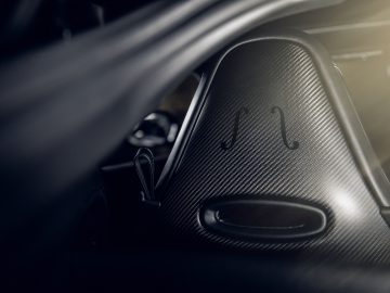 Close-up van het interieur van een Aston Martin 007 Edition-auto, waarbij de nadruk ligt op de rugleuning van koolstofvezel met geïntegreerde hoofdsteunsleuven.