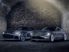 Twee Aston Martin 007 Edition-sportwagens staan naast elkaar geparkeerd in een slecht verlichte bakstenen tunnel.