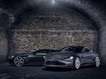 Twee Aston Martin 007 Edition-sportwagens staan naast elkaar geparkeerd in een slecht verlichte bakstenen tunnel.