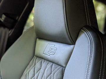 Close-up van een zwartleren Audi A3-autostoeltje met een gewatteerd ontwerp en een 's'-logo in reliëf op de hoofdsteun.
