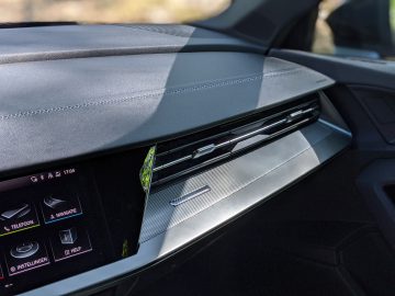 Interieur van een Audi A3 met een dashboard met een digitaal display en ventilatieopeningen, met zilveren afwerking en gedetailleerde stiksels.