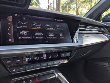 Audi A3-infotainmentscherm met verschillende opties zoals radio, media en navigatie, met daaronder zichtbare dashboardbedieningen.