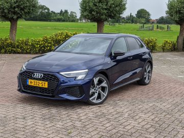 Een Audi A3 geparkeerd op een verhard terrein met een grasveld en gele bloemen op de achtergrond.