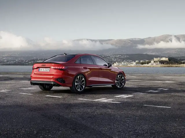 Rode Audi S3 geparkeerd op een leeg perceel met uitzicht op een schilderachtig vergezicht met bergen en wolken op de achtergrond.