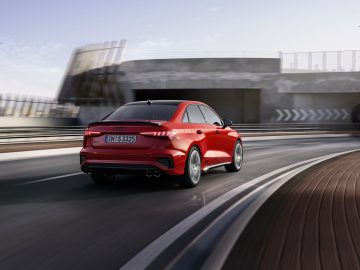 Een rode Audi S3 die over een snelweg rijdt met bewegingsonscherpte-effect op de achtergrond, wat dynamische bewegingen en modern auto-ontwerp laat zien.