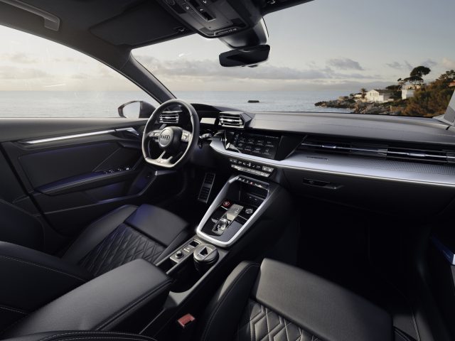Binnenaanzicht van de Audi S3 met strak dashboard, leren stoelen en uitzicht op de oceaan door de voorruit.