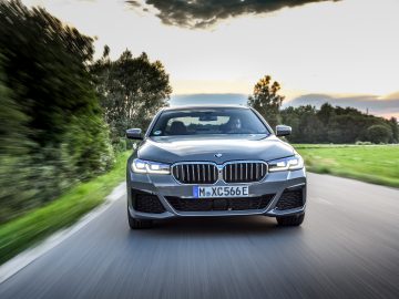 Een zilverkleurige BMW 545e xDrive-serie die in de schemering over een landelijke weg rijdt, met bewegingsonscherpte en een levendige lucht.