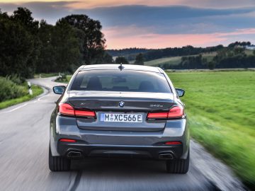 Een BMW 545e xDrive die in de schemering over een bochtige weg door het platteland rijdt, ter illustratie van beweging met een onscherpe achtergrond.