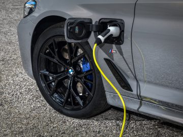 Een BMW 545e xDrive elektrische auto aangesloten op een laadstation, waarbij de nadruk ligt op de laadaansluiting aan de zijkant van het voertuig.