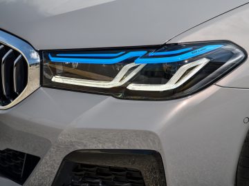 Close-up van de LED-koplamp van een moderne BMW 545e xDrive met ingewikkelde blauwe accenten op een zilveren voertuig.