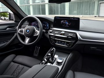 Binnenaanzicht van een BMW 545e xDrive vanaf de bestuurdersstoel, met het stuur, het dashboard en het infotainmentsysteem.