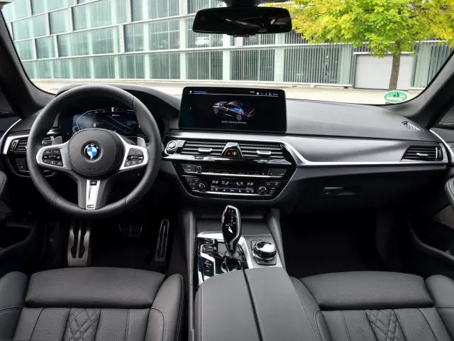 Binnenaanzicht van een BMW 545e xDrive-auto met het stuur, het dashboard met beeldscherm en lederen stoelen.