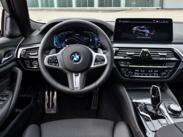Binnenaanzicht van een BMW 545e xDrive-auto met het stuur, het dashboard, de digitale displays en de middenconsole.