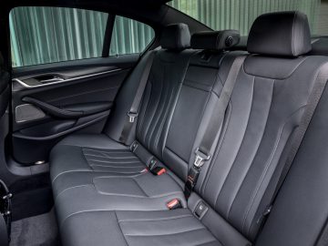 Binnenaanzicht van een BMW 545e xDrive met de achterbank met zwart lederen bekleding, veiligheidsgordels en een deurpaneel met raambediening.