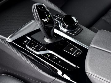 Binnenaanzicht van de middenconsole van een BMW 545e xDrive met versnellingspook, bedieningsknoppen en aanraakgevoelige knoppen.