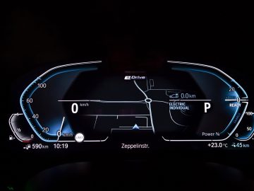 Verlicht digitaal dashboard van een BMW 545e xDrive met nulsnelheid, volle batterij en verschillende voertuigstatusindicatoren.