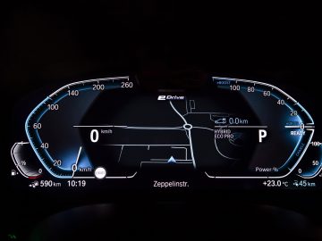 Digitaal dashboard van een BMW 545e xDrive met nul kilometer per uur, parkeerstatus en 's nachts verlichte hybride richtingaanwijzers.