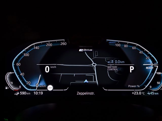 Verlicht digitaal dashboard van een BMW 545e xDrive met snelheidsmeter, batterijniveau en andere voertuigstatusindicatoren 's nachts.