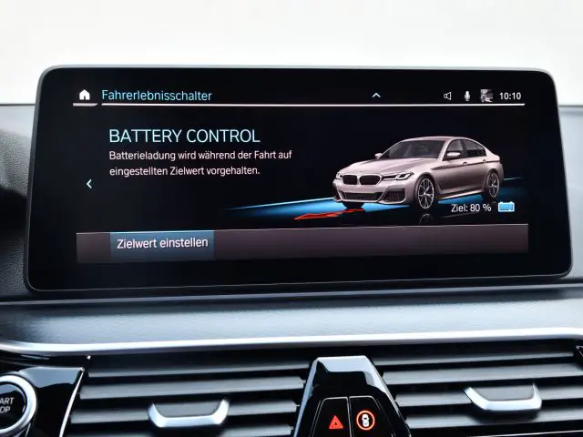 Auto-interieur met een BMW 545e xDrive dashboarddisplay met een "batterijcontrole" -scherm in het Duits, met een afbeelding van een auto en instellingen voor het opladen van de batterij.