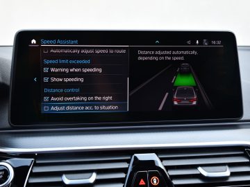 Autodashboard van de BMW 545e xDrive met een snelheidsassistentinterface op het centrale touchscreen, met verschillende rij-instellingen zichtbaar.