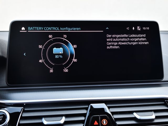 Autodashboard met een BMW 545e xDrive-batterijcontrolescherm met een laadniveau-instelling van 80%, vergezeld van een Duitse tekst met uitleg over automatisch laadonderhoud.