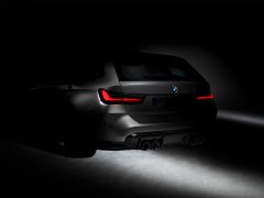 Achteraanzicht van een grijze BMW M3-auto verlicht met rode achterlichten in een slecht verlichte omgeving, wat het strakke ontwerp en de dubbele uitlaatpijpen benadrukt.