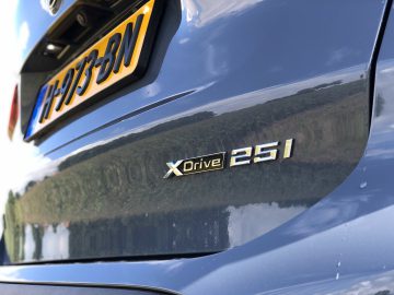 Close-up van de achterkant van een BMW X1 xDrive25i met een reflecterend oppervlak met de "xDrive 25i" -badge en het kenteken met de tekst "FH57 BJY".