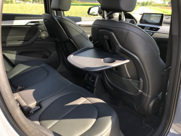 Binnenaanzicht van de BMW X1 xDrive25i met de voorstoelen en een open dienblad aan de achterkant van de passagiersstoel.
