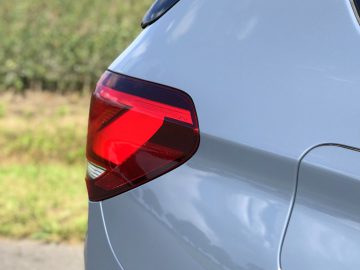 Close-up van het rode achterlicht van een blauwe BMW X1 xDrive25i, met focus op het ingewikkelde ontwerp van de lamp, tegen een wazige groene achtergrond.