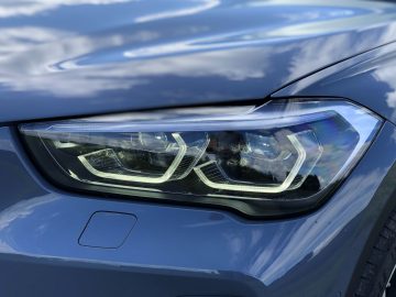 Close-up van de koplamp van een BMW X1 xDrive25i met ingewikkelde led-ontwerpen op een modern blauw voertuig.
