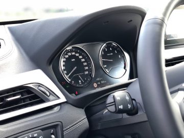 BMW X1 xDrive25i dashboard met stuur, snelheidsmeter, toerenteller en brandstofmeter met verschillende verlichte waarschuwingslampjes.