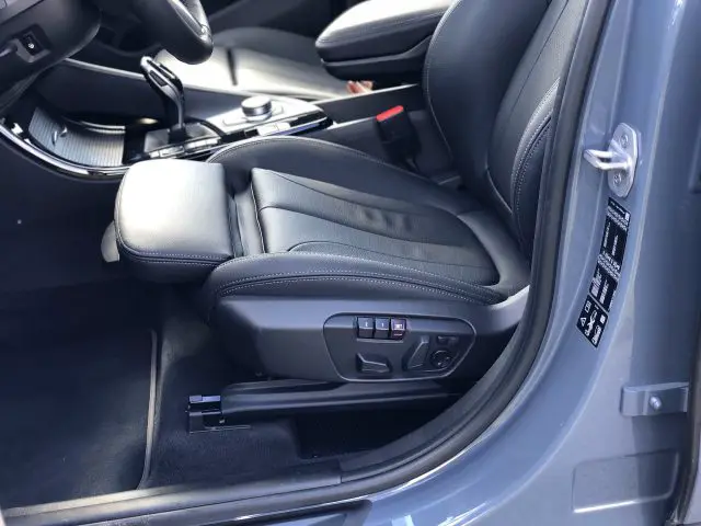 Binnenaanzicht van de BMW X1 xDrive25i met een zwartleren bestuurdersstoel met elektronische verstelknoppen aan de zijkant.