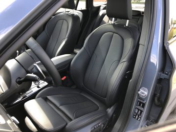 Binnenaanzicht van de BMW X1 xDrive25i met zwartleren stoelen, een versnellingspook en deurbediening.