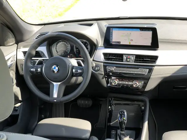 Interieur van een BMW X1 xDrive25i-auto met het stuur, het dashboard en het infotainmentsysteem op een zonnige dag.
