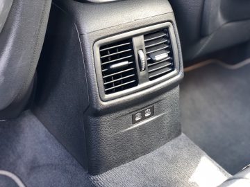 Auto-interieur van een BMW X1 xDrive25i met ventilatieopeningen achterin en bedieningselementen voor stoelverwarming op een middenconsole tussen de stoelen.