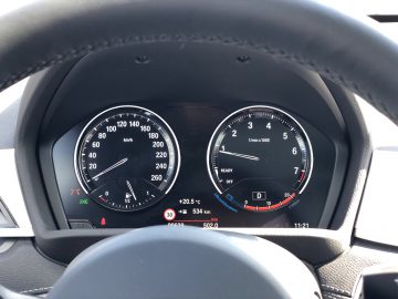 Autodashboard van een BMW X1 xDrive25i met een snelheidsmeter en toerenteller, met zichtbare indicatoren voor temperatuur, versnelling en brandstof.
