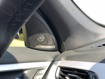 Close-up van een autoluidspreker van Harman Kardon geïnstalleerd in het deurpaneel van een BMW X1 xDrive25i, gezien vanuit het perspectief van de bestuurder.